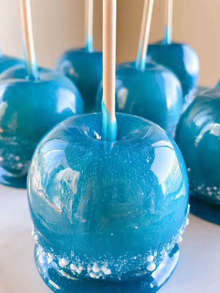 A row of vibrant blue candy apples on a simple surface, showing the translucent blue coating and wooden handles.