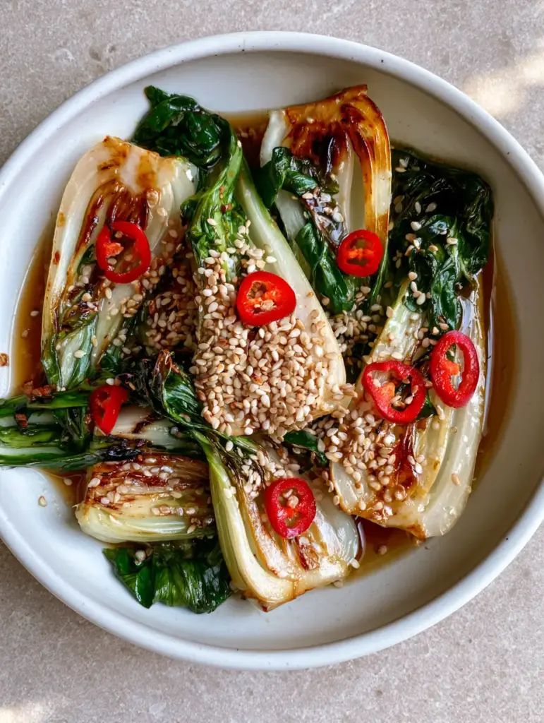 Sautéed Bok Choy with Ginger, Garlic, and Red Chili 1 Sautéed Bok Choy coated in a thin glossy brown sauce, garnished with toasted white sesame seeds and bright red chili peppers.