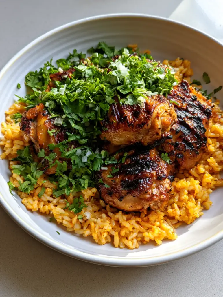 Close up of charred chicken thighs with a citrus marinade glaze on top of seasoned yellow rice. (Angel Chicken Rice Casserole)