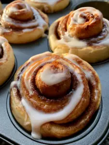 Individual cinnamon roll muffins showing tight spirals of yeast dough and dark brown cinnamon filling.
