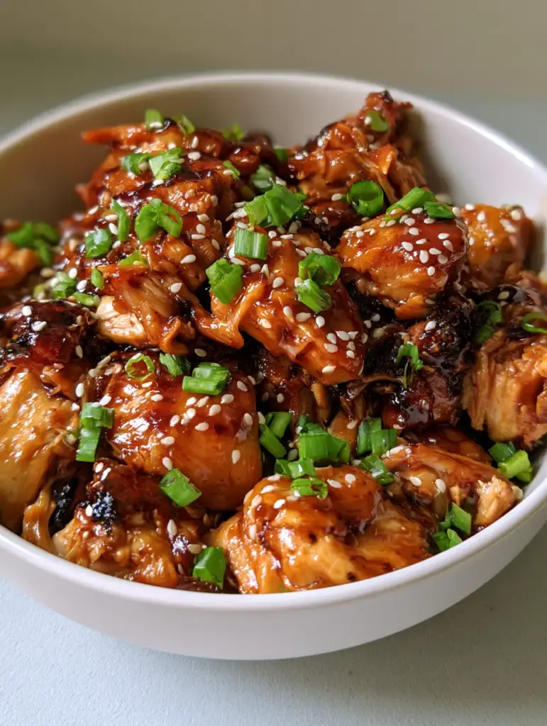 Slow Cooker Chicken Thighs with a Glossy Honey Garlic Glaze 1 Handheld photo showing a white ceramic bowl of Slow Cooker Chicken Thighs garnished with vibrant green scallions.