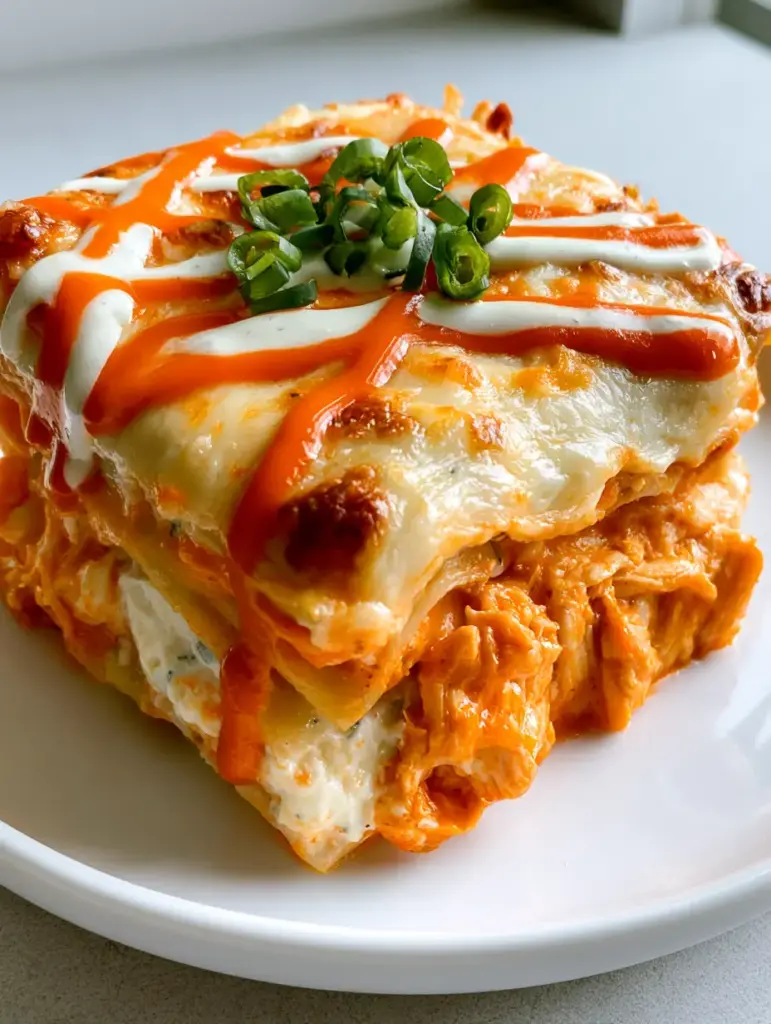 Buffalo Chicken Lasagna: The Ultimate Creamy and Spicy Comfort Food 1 A square serving of Buffalo Chicken Lasagna on a white plate showing the distinct orange and white layers and a ranch criss-cross drizzle.