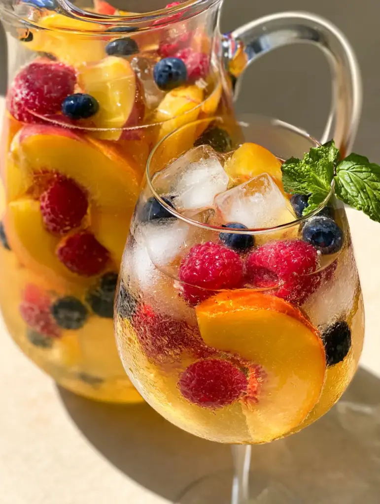 Peach Moscato Sangria: The Ultimate Refreshing Summer Cocktail 2 Close up of Peach Moscato Sangria in a stemmed wine glass with large clear ice cubes and vibrant summer fruit.