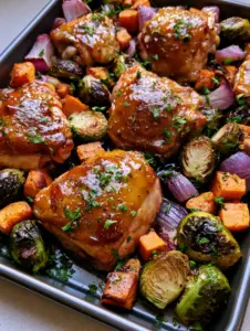 Close up view of glossy honey dijon chicken skin and charred brussels sprouts on a sheet pan. (Sheet Pan Honey Dijon Chicken)