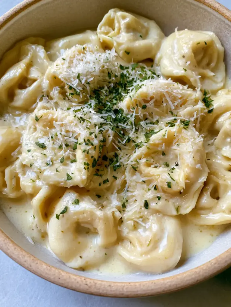 Macro shot of plump tortellini pillows generously coated in a pale-cream garlic butter sauce with green parsley flakes.